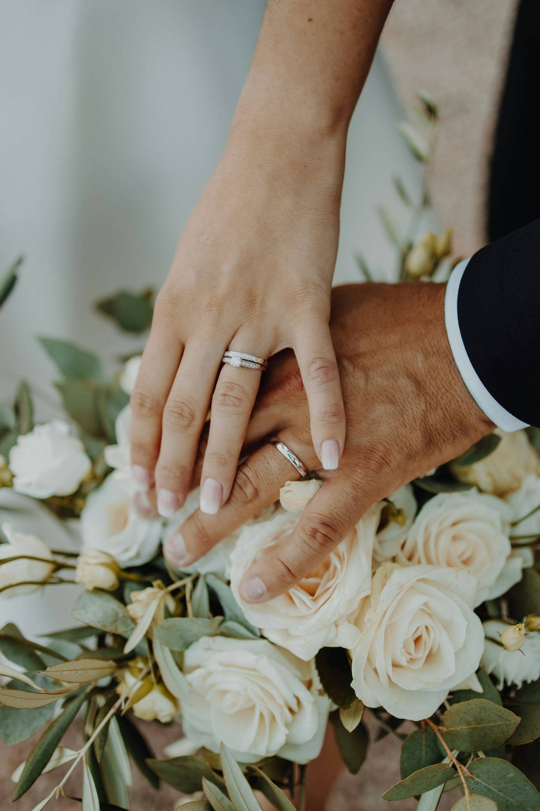 Les mains des mariés et leurs alliances posées sur un bouquet de roses blanches