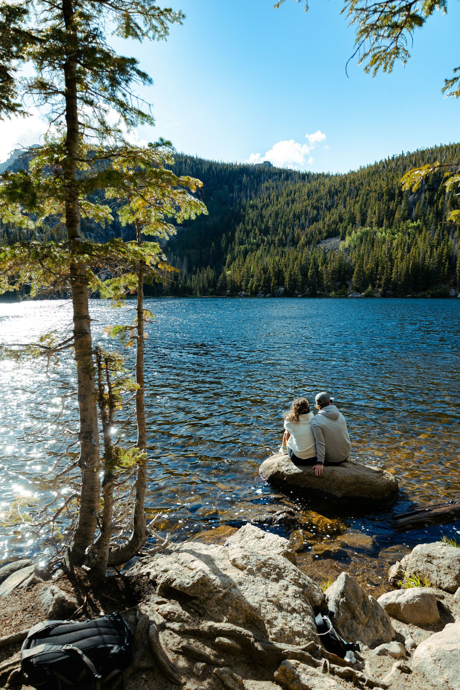 Un couple assis sur un rocher au bord d’un lac de montagne, entre les sapins