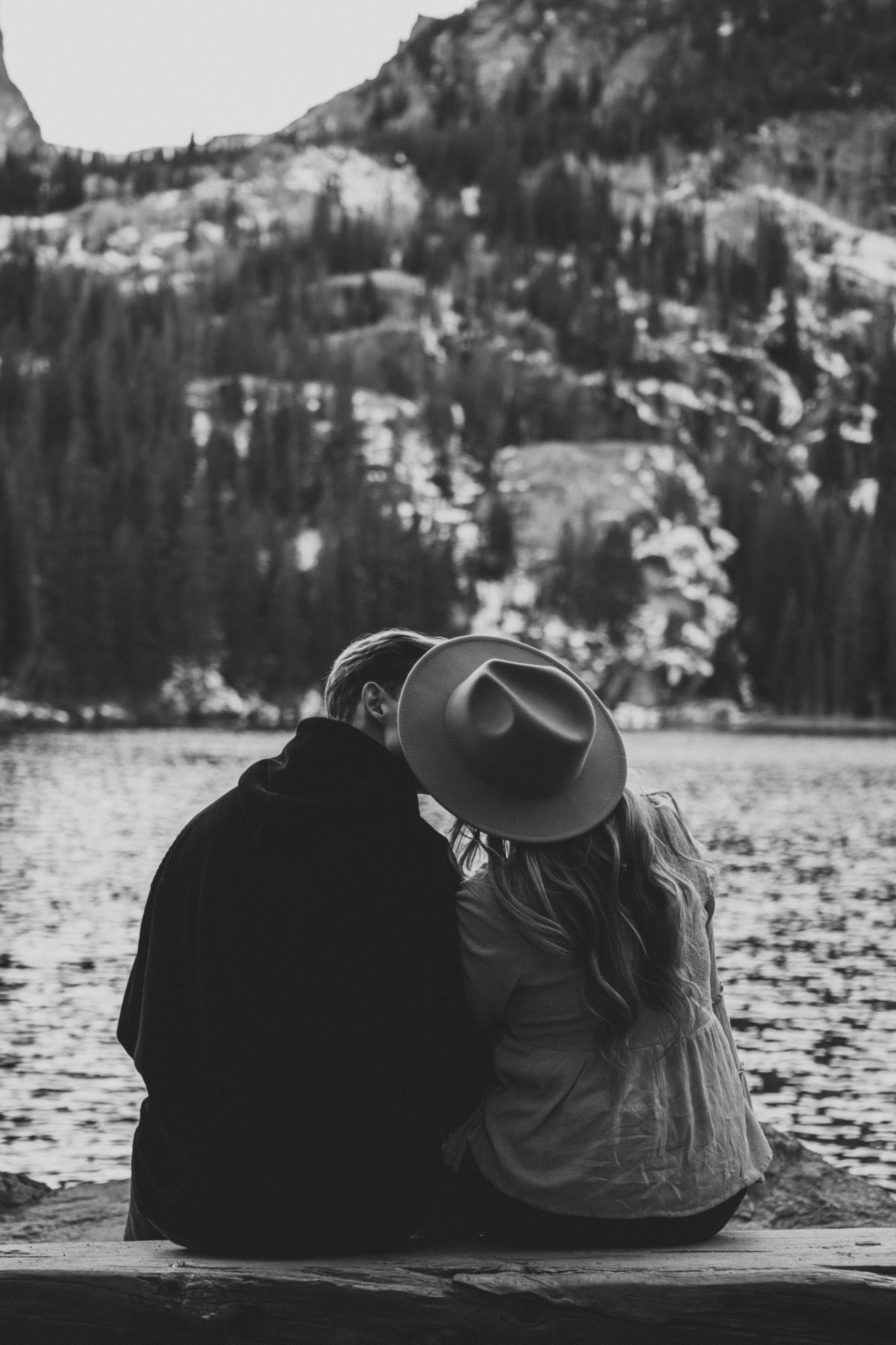 En noir et blanc, un couple de dos, serré l’un contre l’autre face au lac