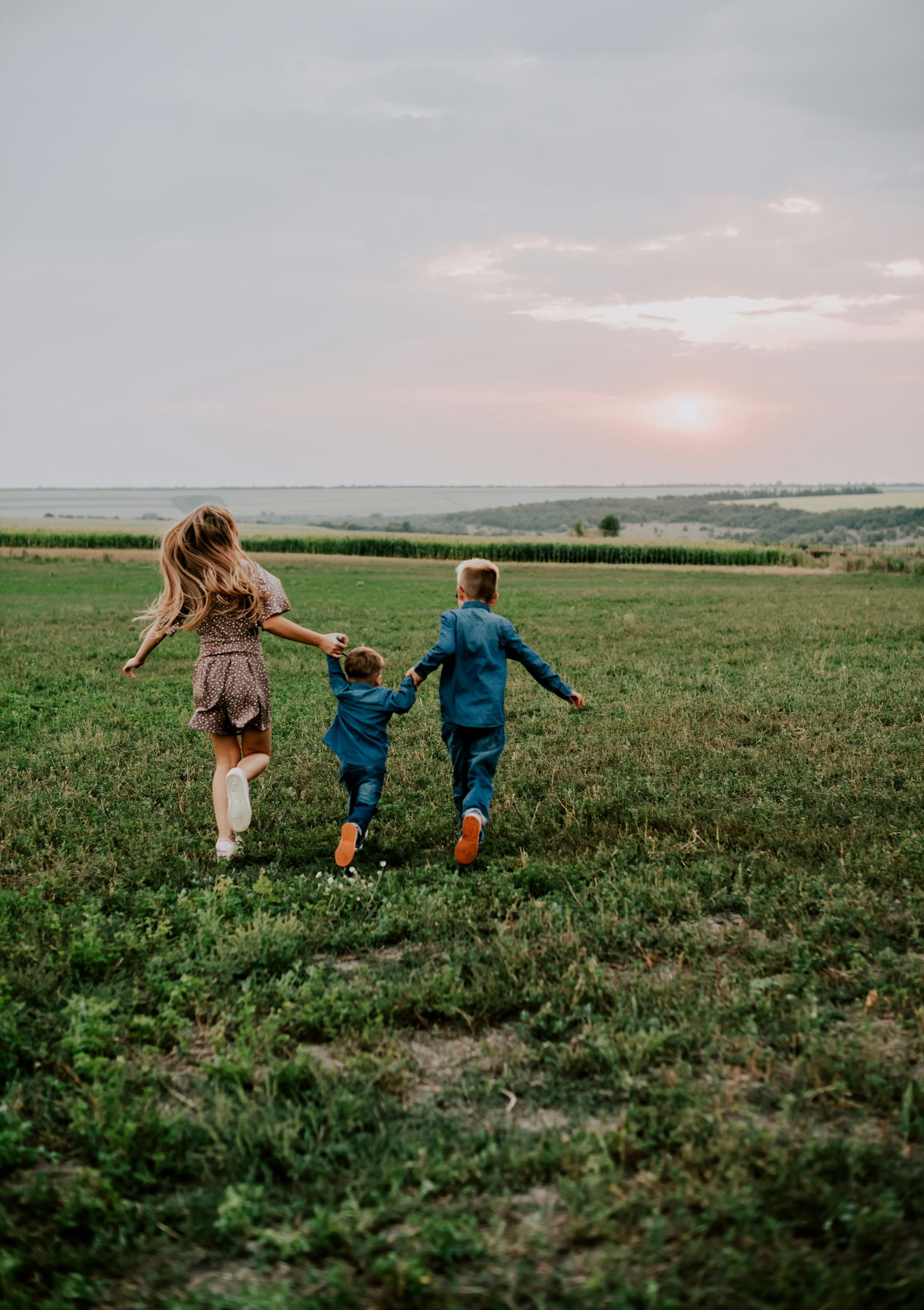 Trois enfants courent dans l’herbe vers l’horizon, main dans la main