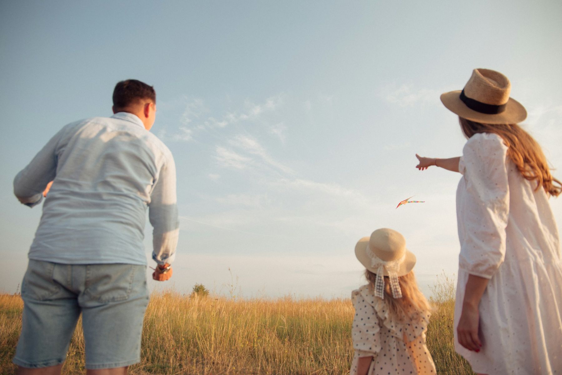 Des parents et leur petite fille en chapeau de paille regardent le ciel dans un champ
