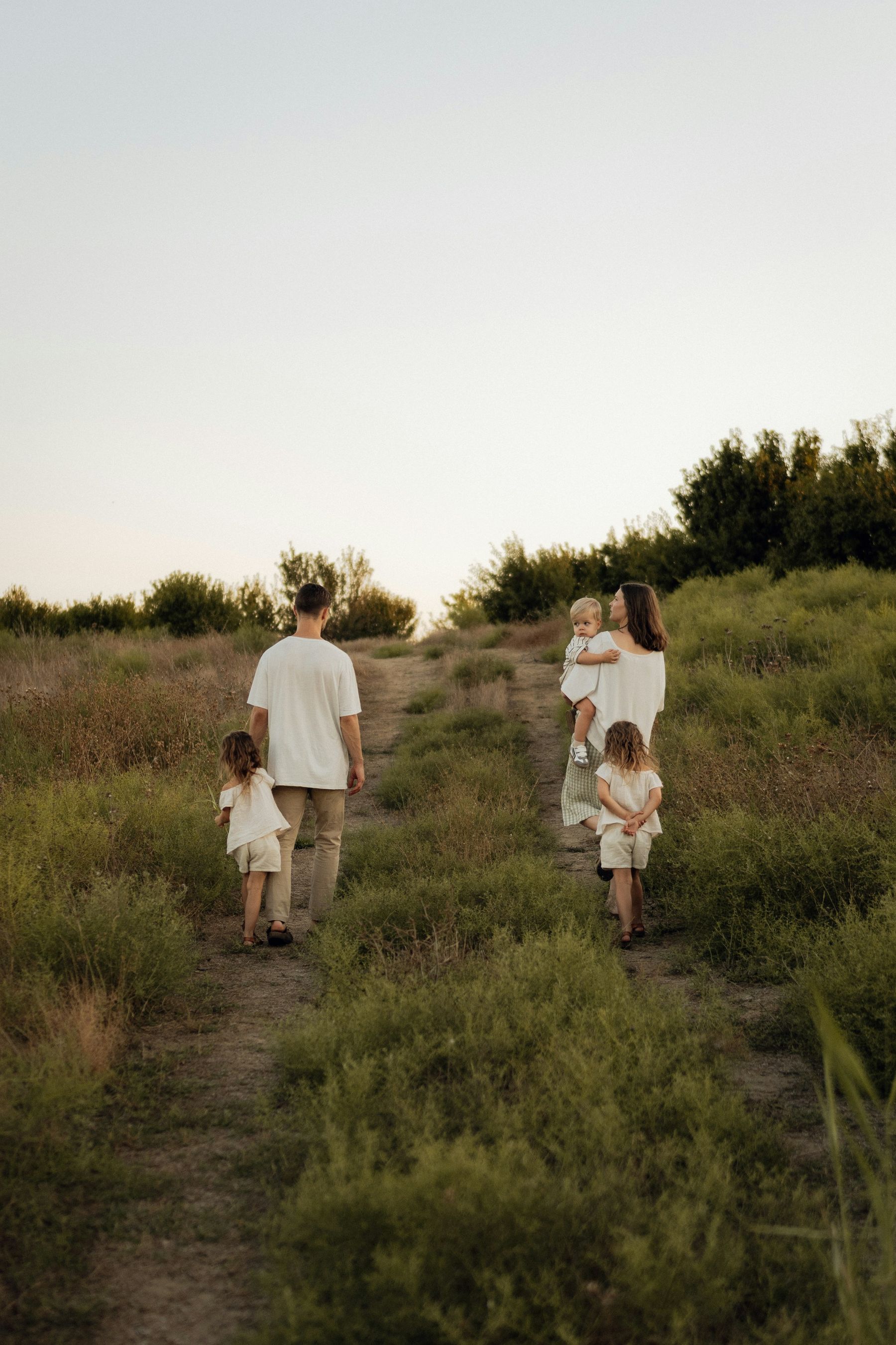 Une famille marche de dos sur un chemin dans les hautes herbes, en fin de journée