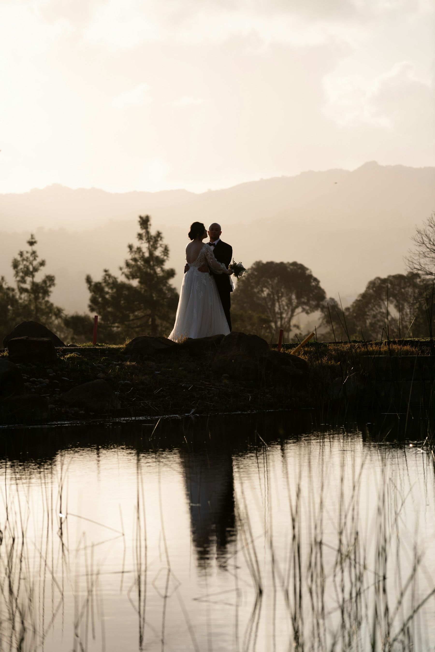 Les mariés à contre-jour au bord de l’eau, leur reflet dans le lac au coucher du soleil